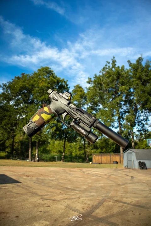 Handgun with a cylindrical barrel attachment photographed against a blue sky
