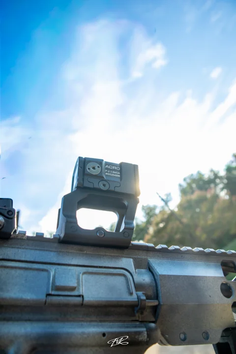 Close-up of a firearm optic and upper receiver in sunlight